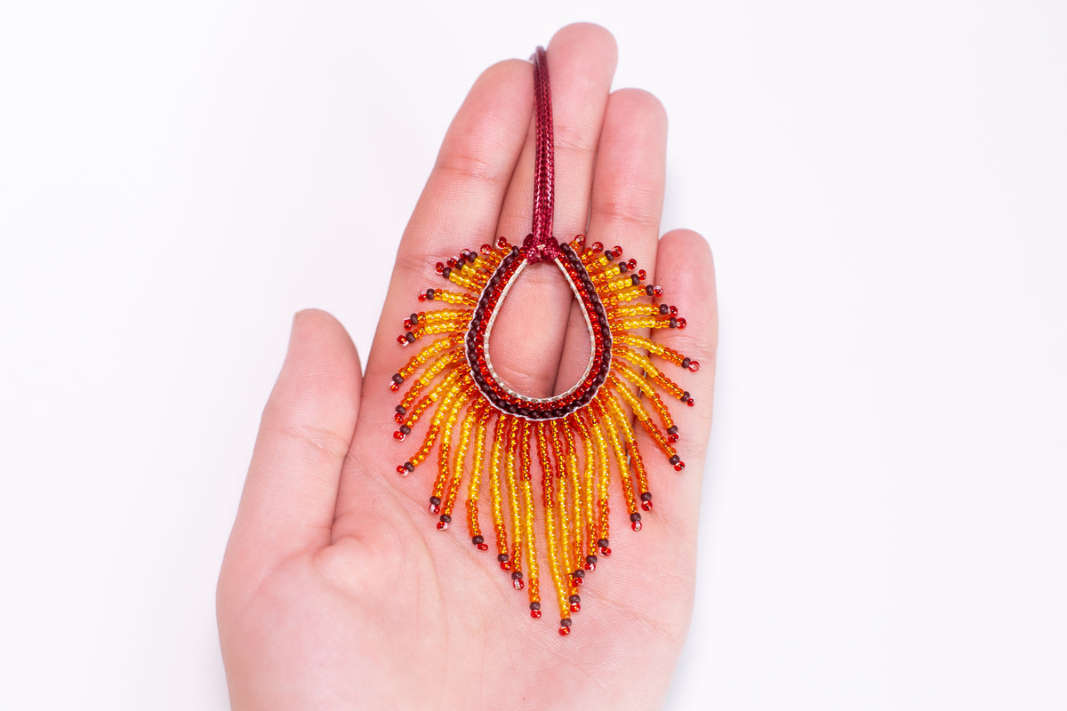 A hand holding a colorful beaded necklace with a sunburst design.