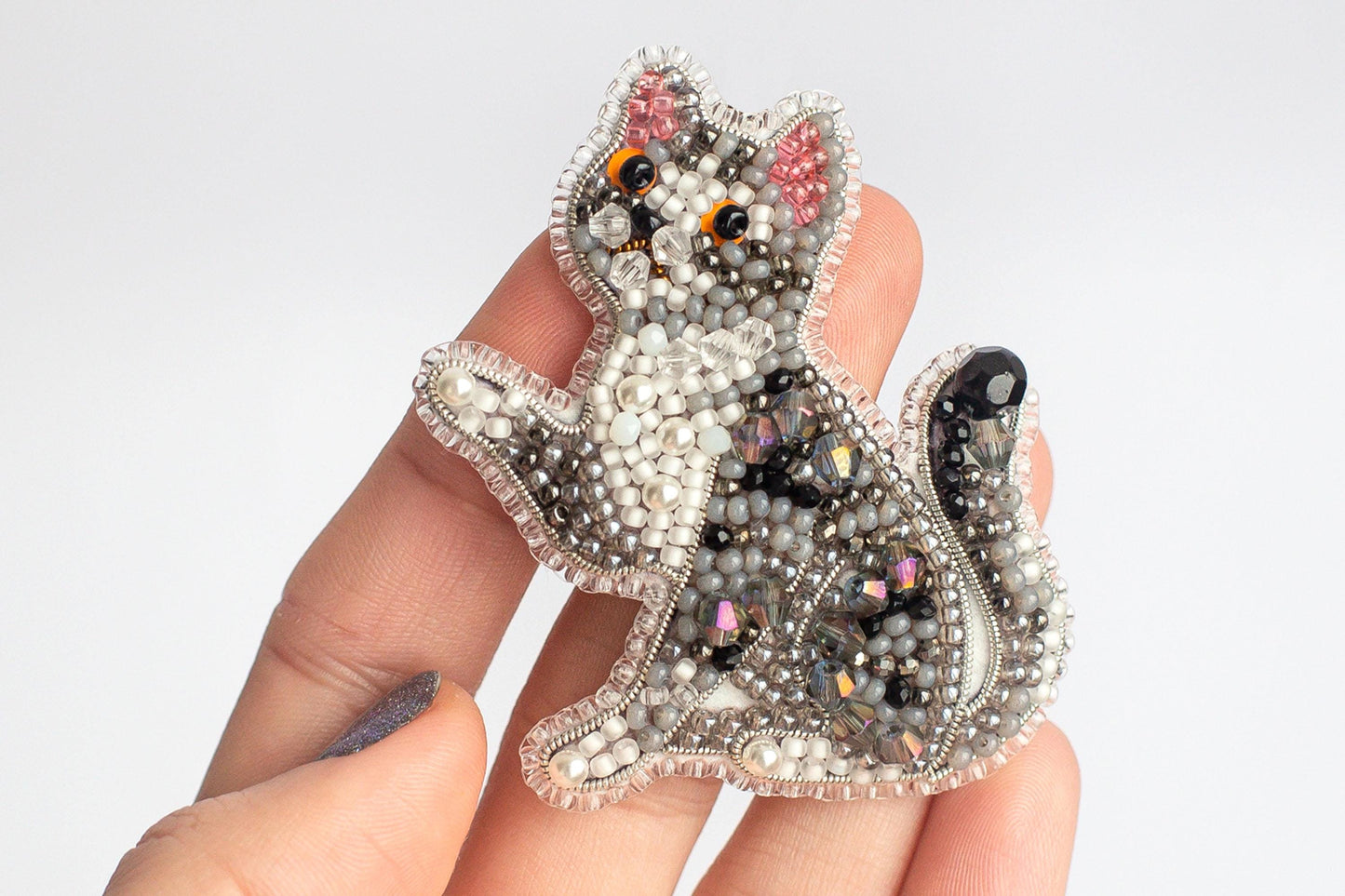 A hand holding a decorative beaded cat pin.