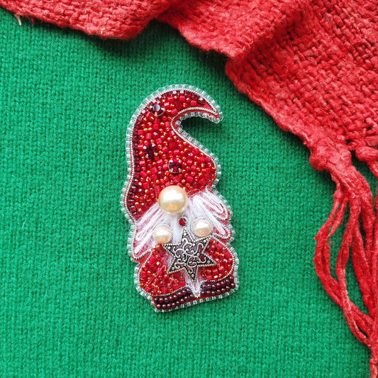 A red knitted scarf with a red and silver ornament is placed on a green background.