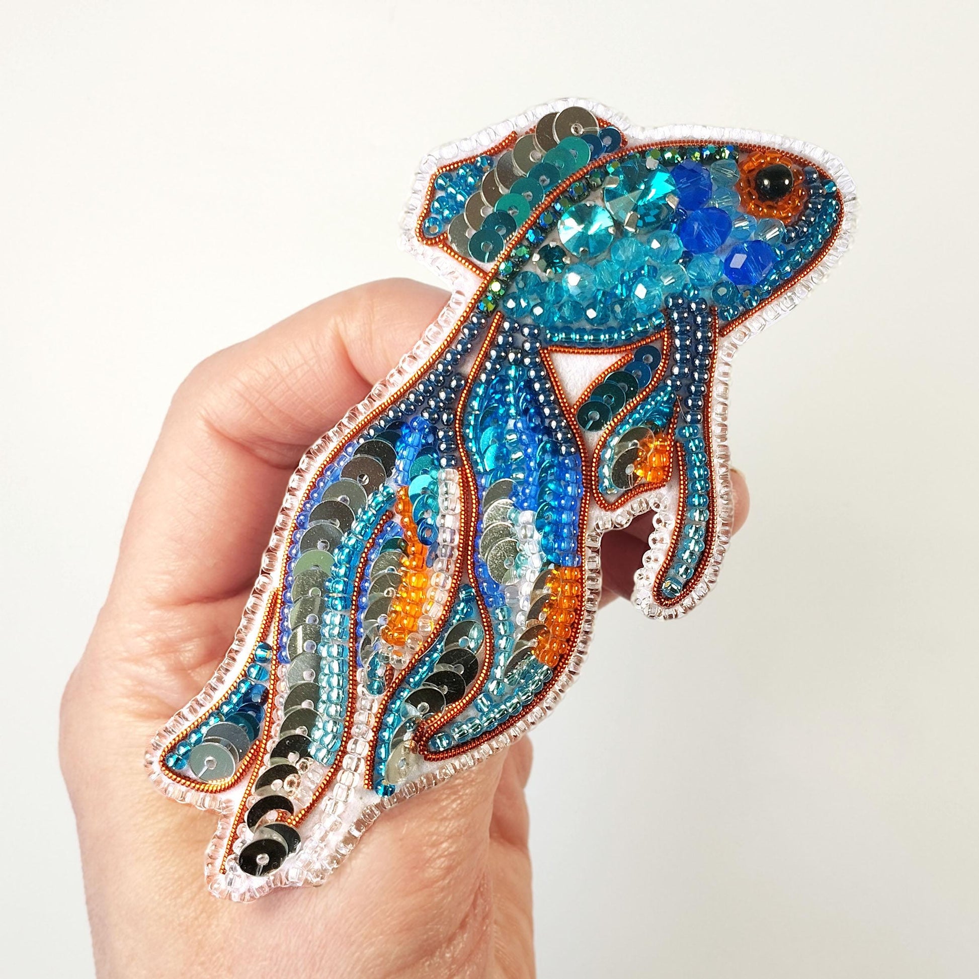 a hand holding a colorful fish brooch with sequins