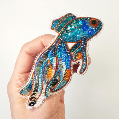 a hand holding a colorful fish brooch with sequins