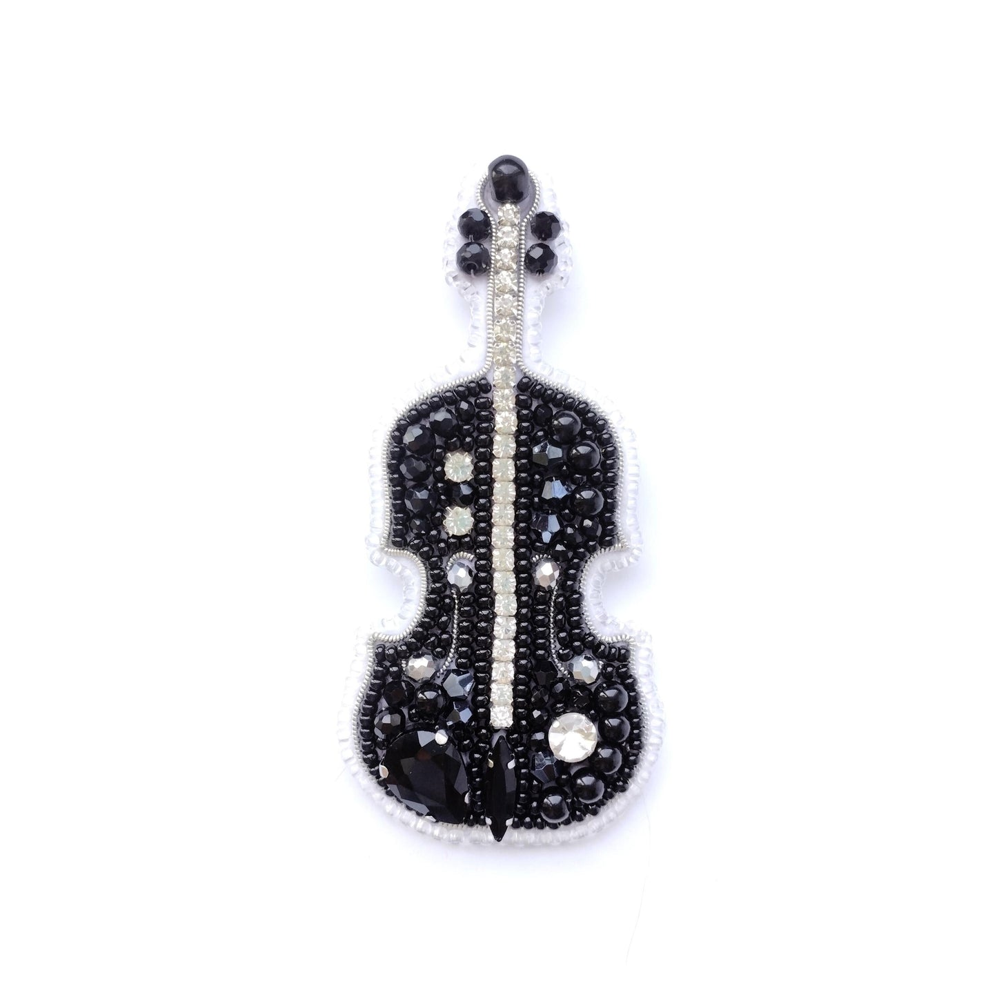 A black and white embroidered brooch or pin featuring a violin design, adorned with numerous small rhinestones or crystals.
