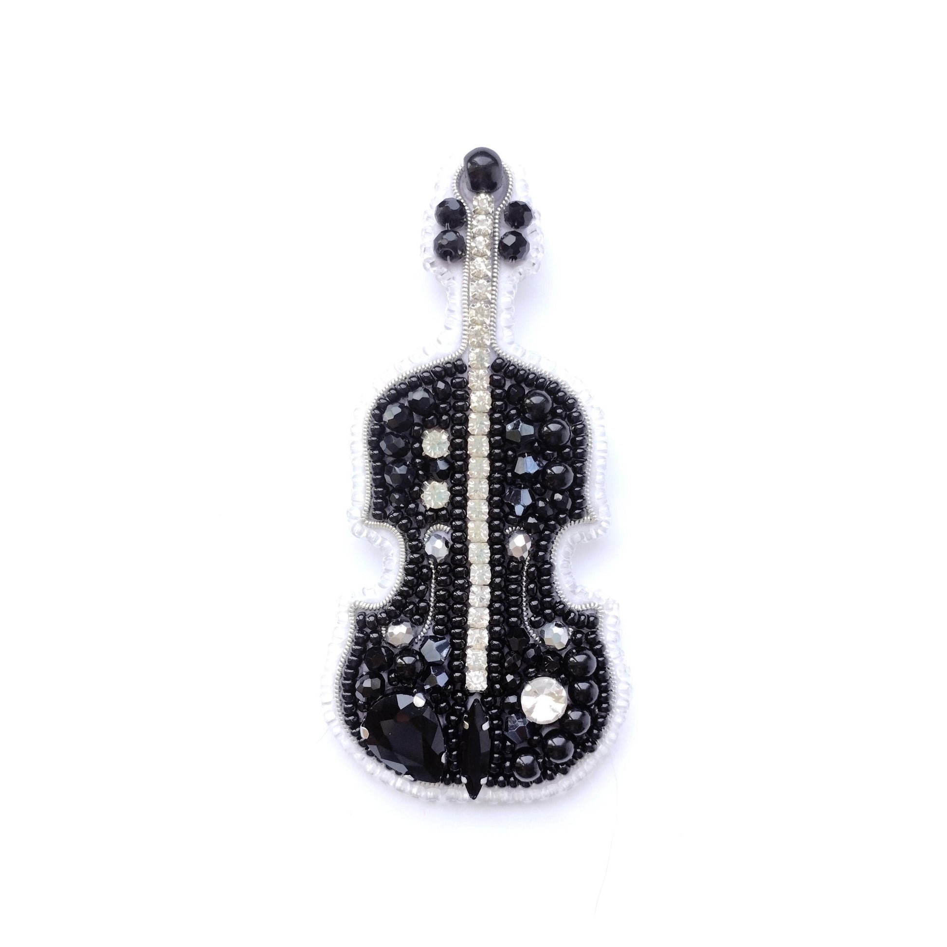 A black and white embroidered brooch or pin featuring a violin design, adorned with numerous small rhinestones or crystals.