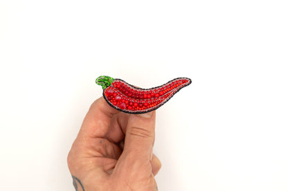 a hand is holding a red beaded brooch