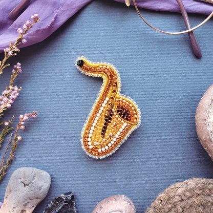 a close-up of a beaded object resembling a saxophone, surrounded by various objects such as a pair of glasses, a purple cloth, and some rocks.