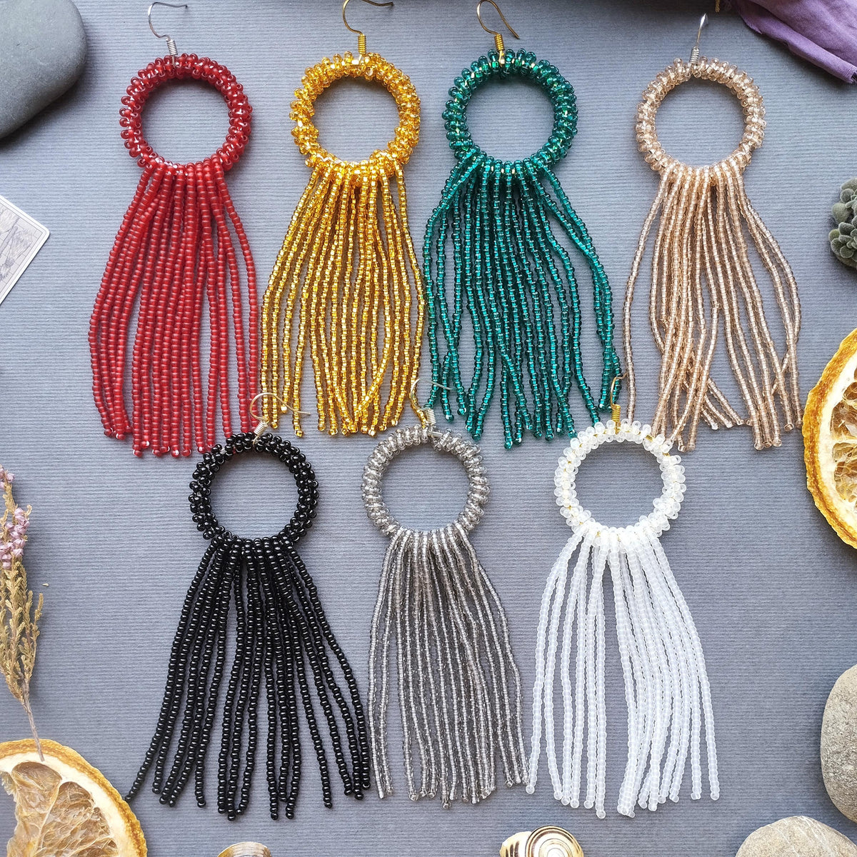 A collection of colorful beaded earrings with long tassels, arranged on a gray background.