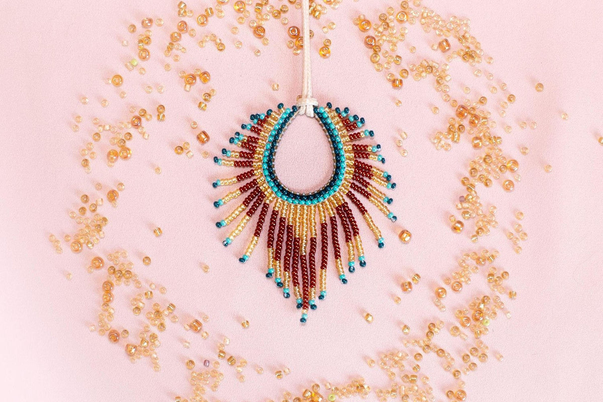 a beaded necklace with a large, colorful pendant, surrounded by scattered beads in various shades of gold, red, and blue.