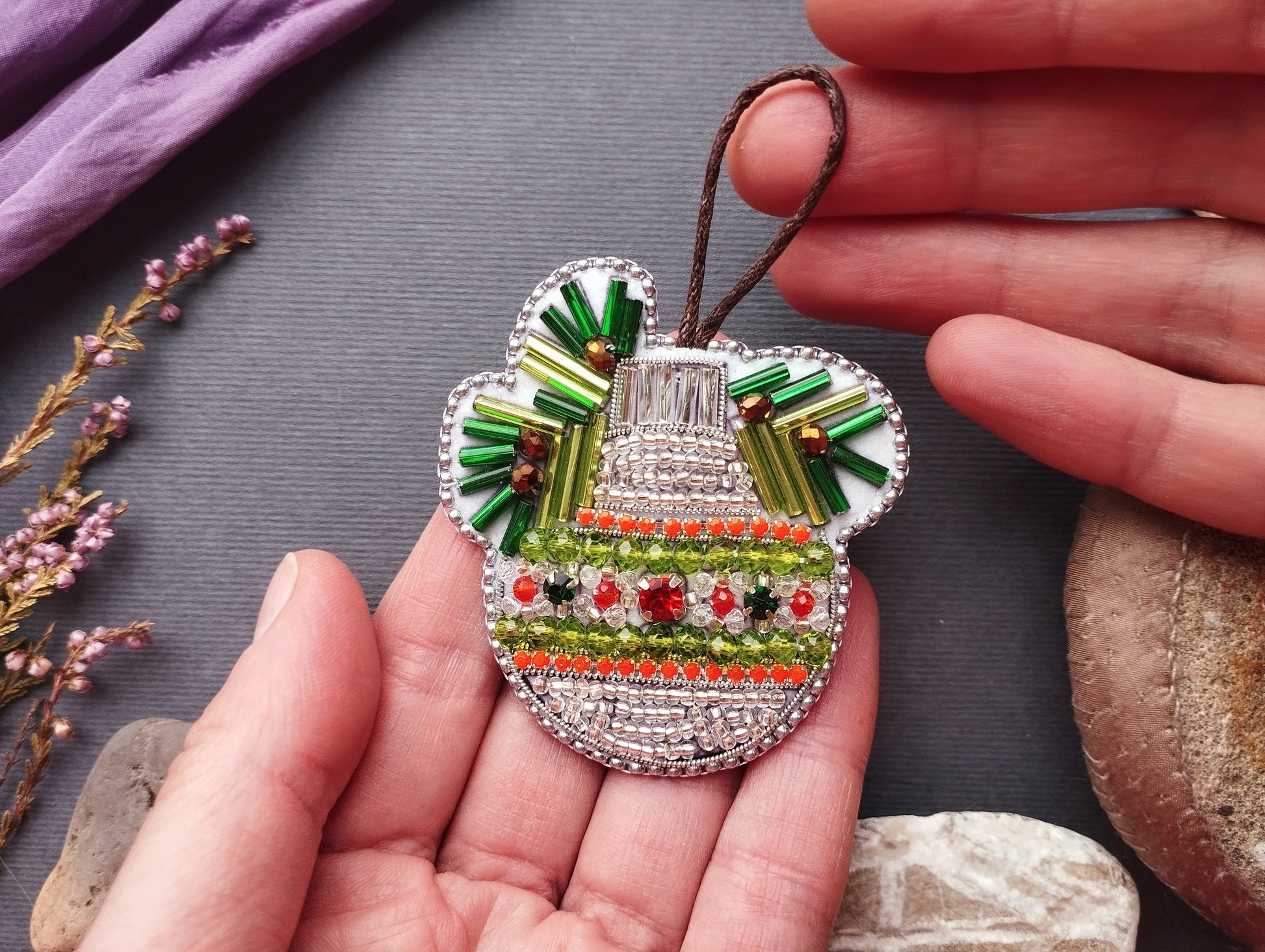 A hand holding a decorative ornament made of colorful beads and wire, with a floral pattern.