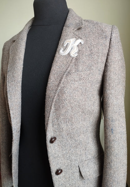 A gray tweed blazer with a white "K" embroidered on the left side, displayed on a mannequin.
