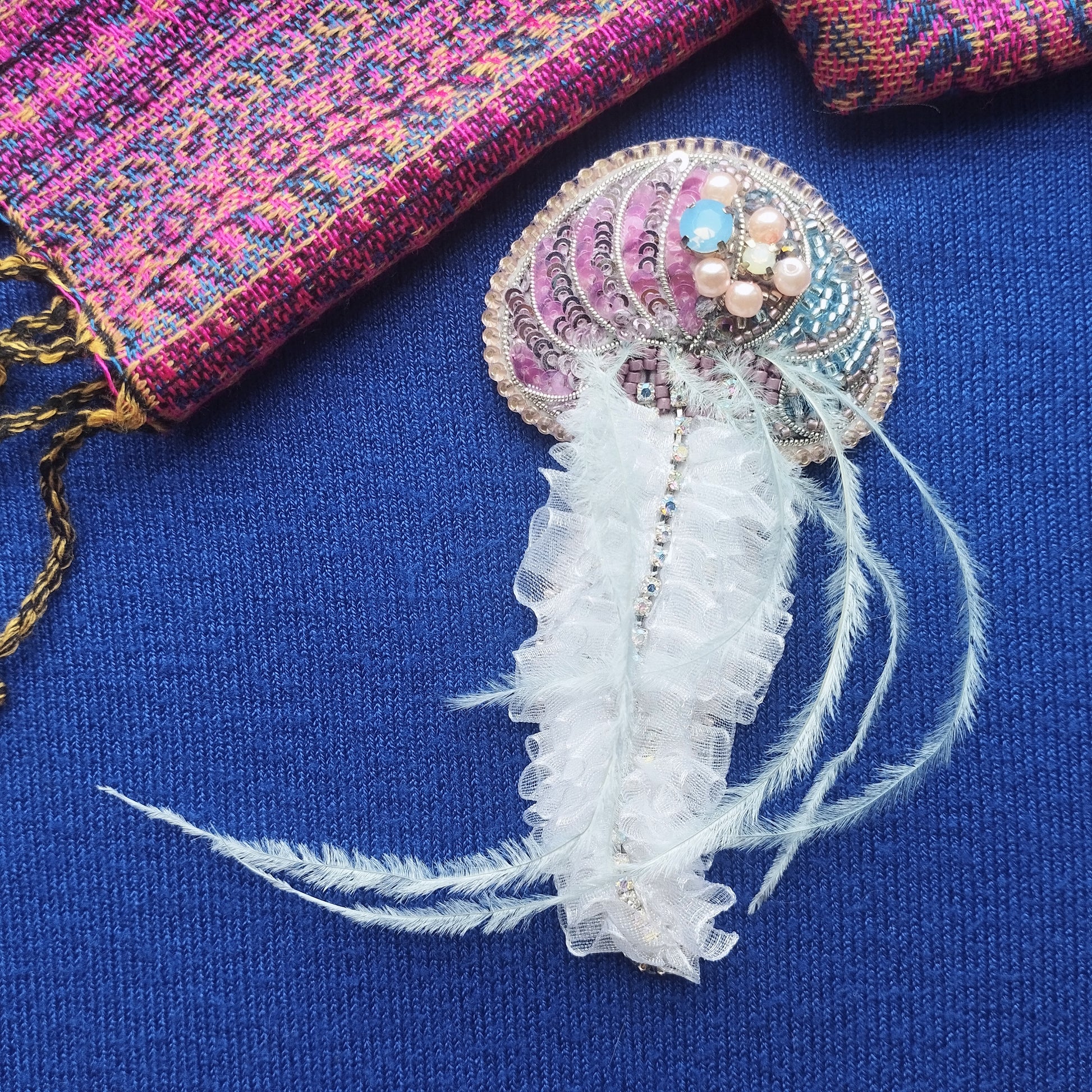 a decorative piece with a ruffled white feather and a beaded design, placed on a blue fabric background.