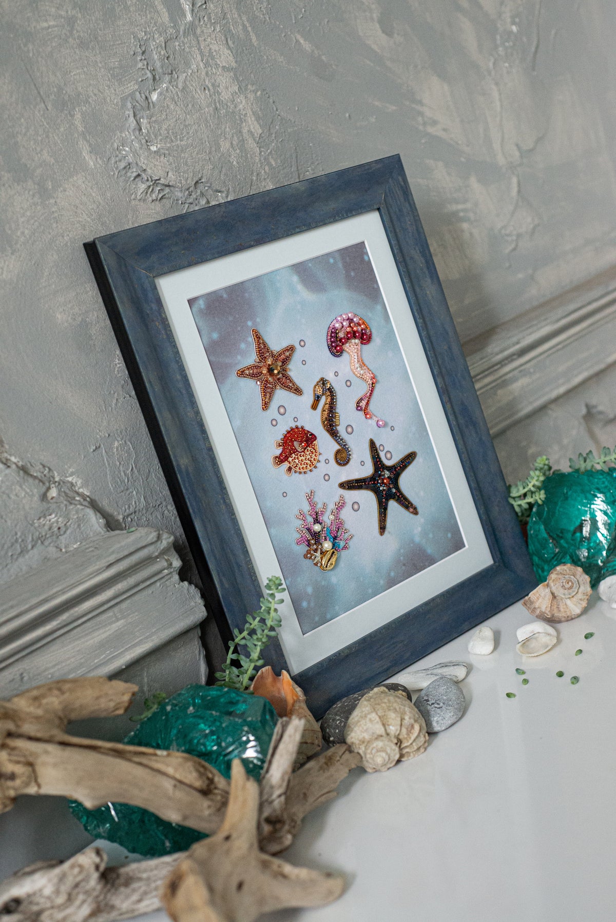 A framed artwork depicting various marine life, including a starfish, jellyfish, and seahorse, is displayed on a shelf alongside other decorative items.
