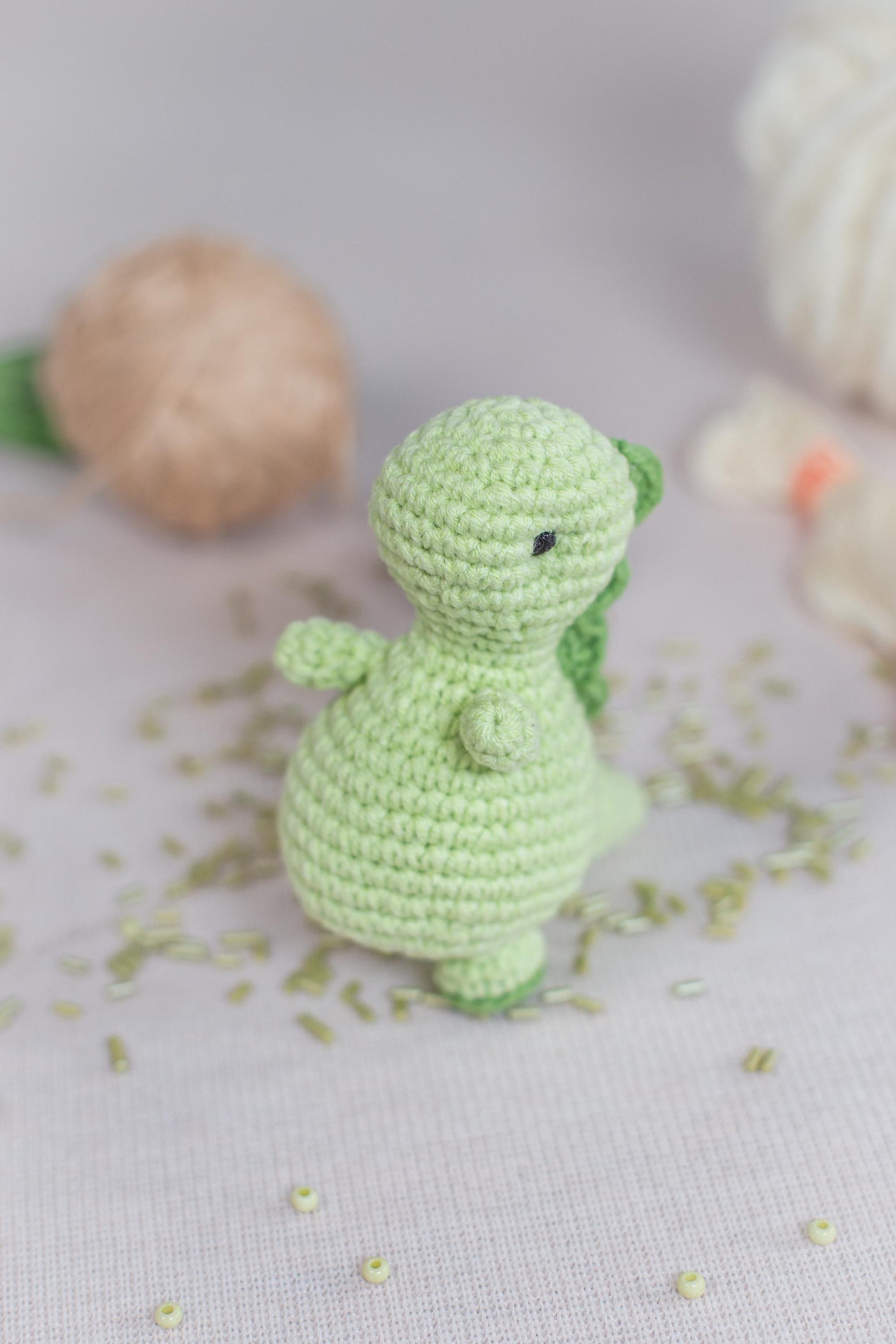 a small crocheted green dinosaur sitting next to a ball of yarn