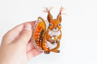 A hand holding a decorative beaded squirrel pin.