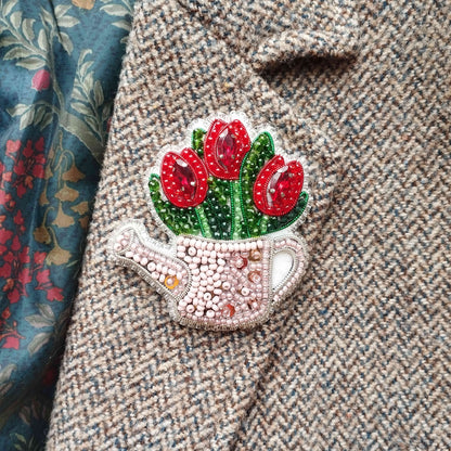 A close-up of a beaded, embroidered pin or brooch on a tweed jacket, featuring a design of red flowers.