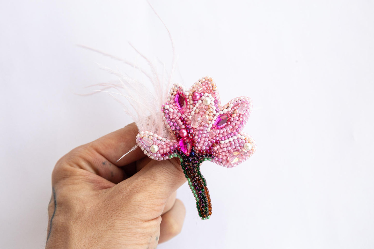 a hand holding a beaded flower with feathers