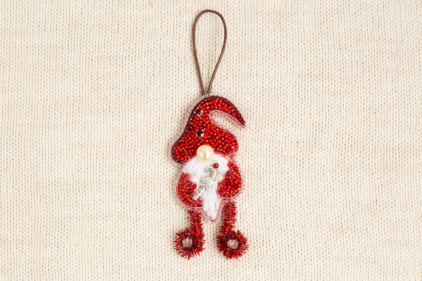 A red ornament resembling a gnome or gnome-like figure is hanging on a beige background.