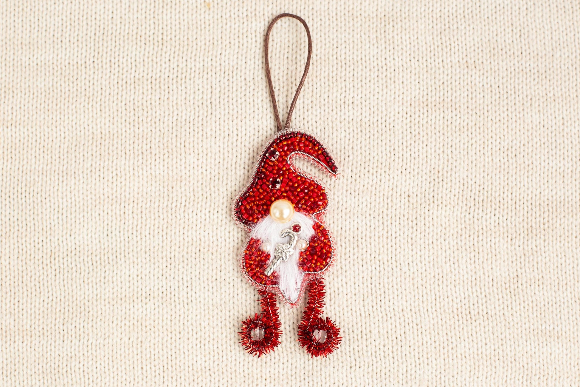 A red ornament resembling a gnome or gnome-like figure is hanging on a beige background.