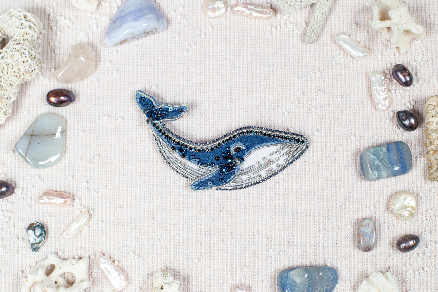 a blue whale surrounded by various sea-themed objects, including pearls, gemstones, and coral, all arranged on a light-colored background.