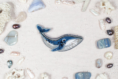 a blue whale surrounded by various sea-themed objects, including pearls, gemstones, and coral, all arranged on a light-colored background.