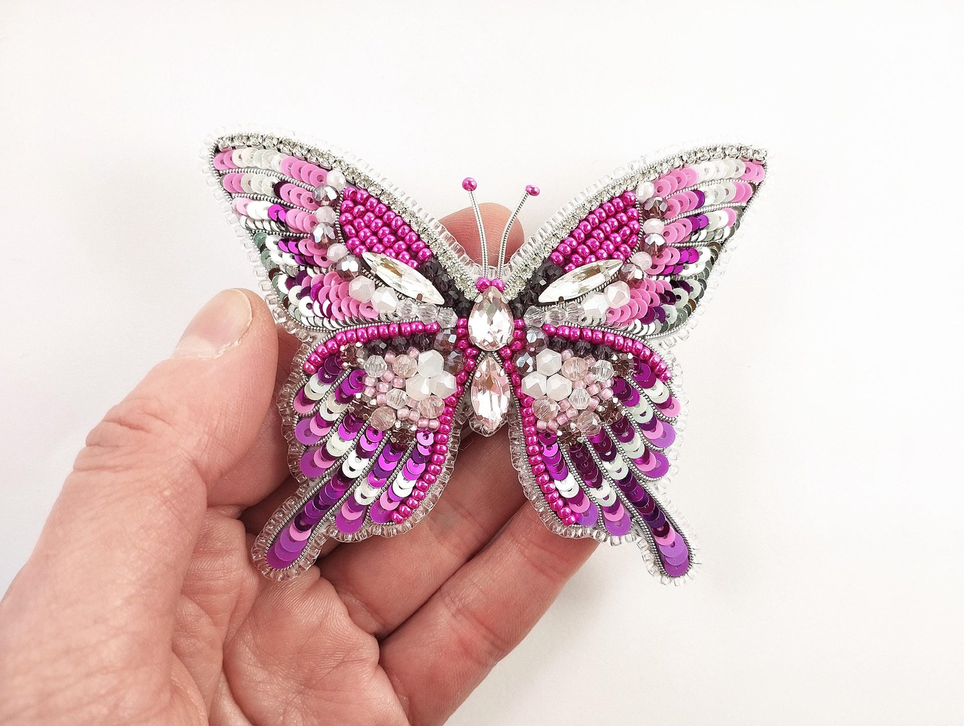 a hand holding a pink and silver butterfly brooch