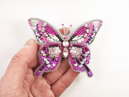a hand holding a pink and silver butterfly brooch