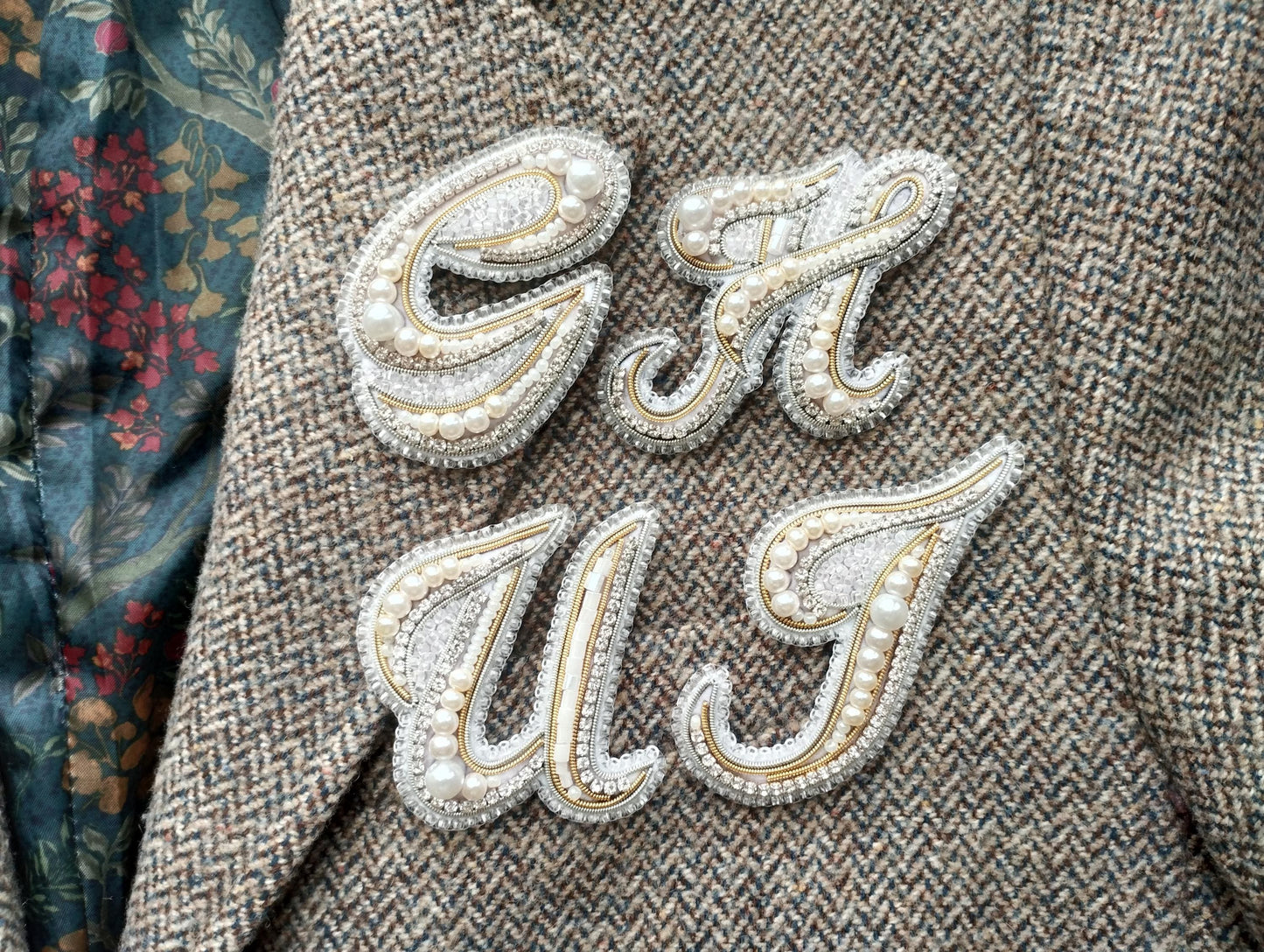 a close-up of a fabric with a decorative embroidered letter "C" and "U" attached to it, both embellished with pearls and rhinestones.