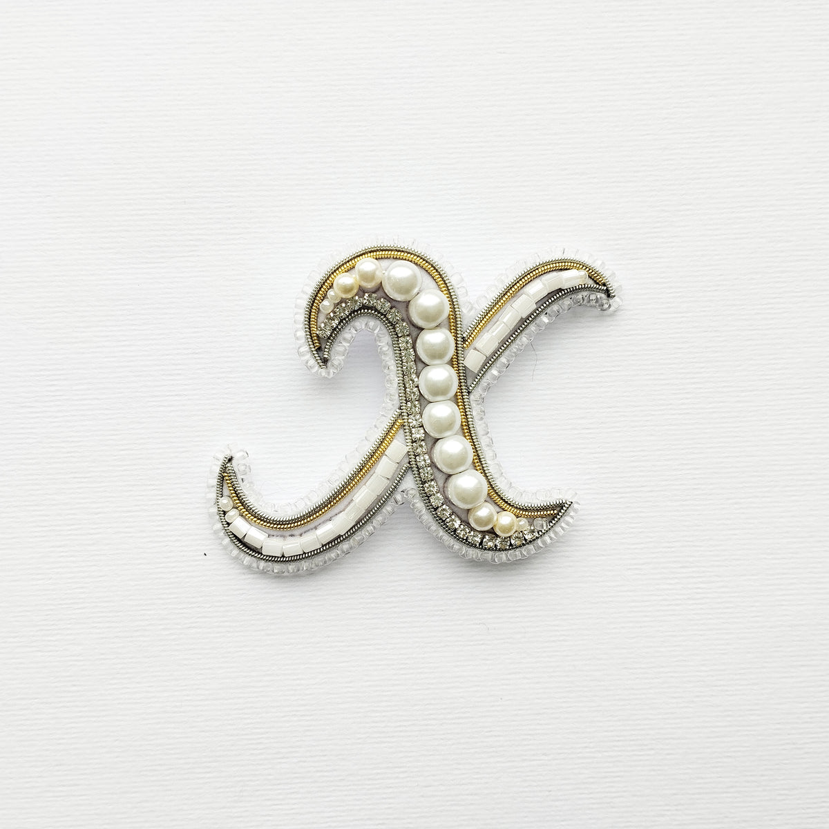 a decorative letter 'X' made of beads and pearls, set against a plain white background.