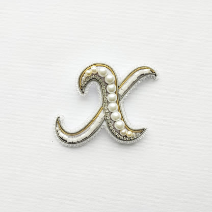 a decorative letter 'X' made of beads and pearls, set against a plain white background.