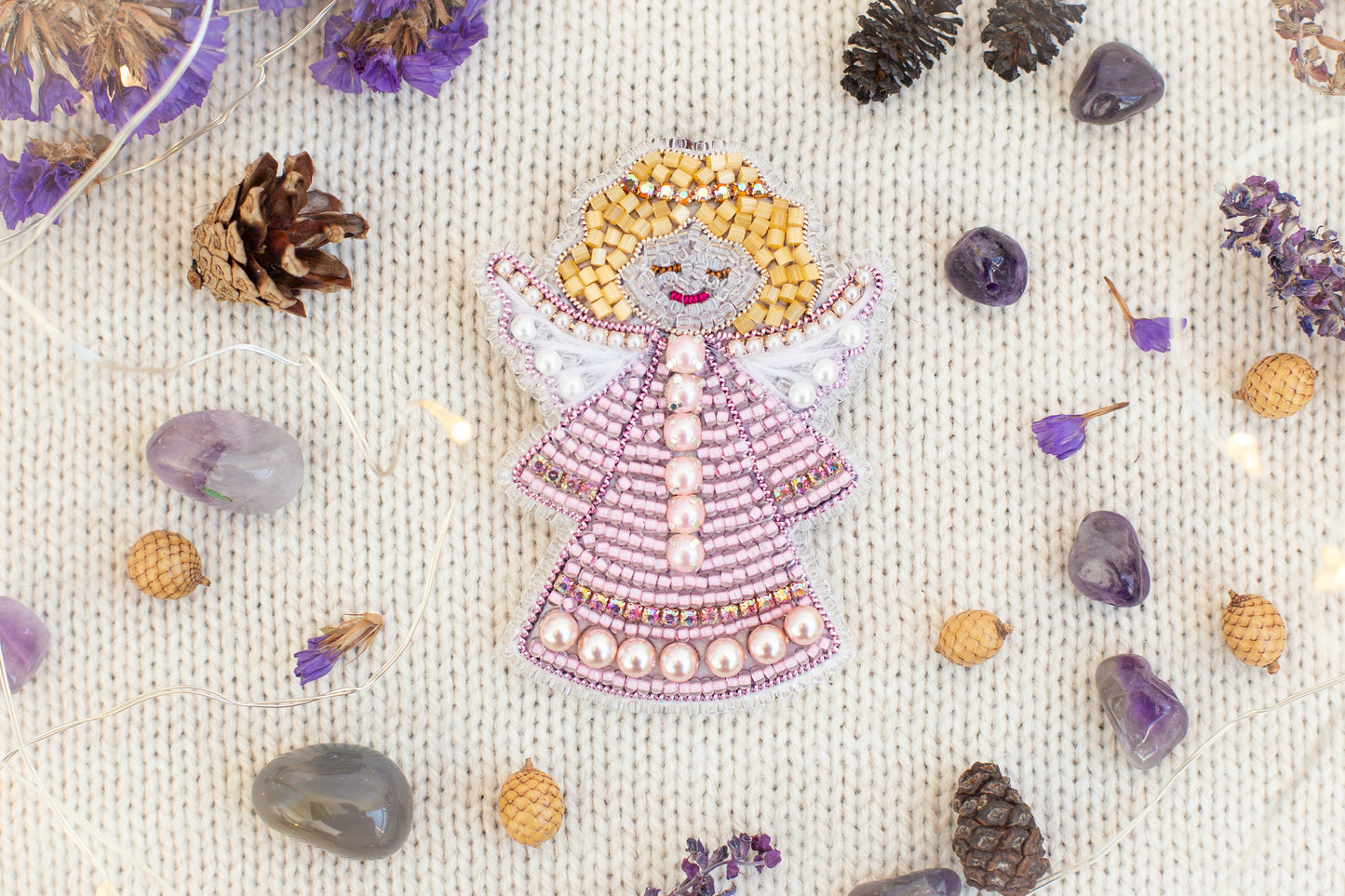 a decorative angel figure made of beads and surrounded by various natural elements, such as pine cones, gemstones, and flowers.