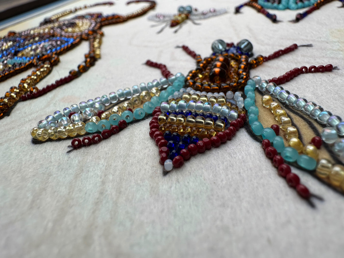 a close-up view of a detailed embroidered design on a fabric surface, showcasing a variety of colorful beads and beads arranged in a pattern resembling insects or other small creatures.