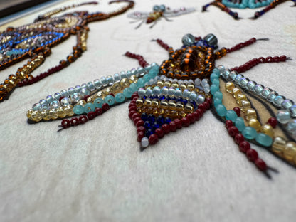a close-up view of a detailed embroidered design on a fabric surface, showcasing a variety of colorful beads and beads arranged in a pattern resembling insects or other small creatures.