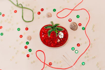 a close-up view of a red and green bead-like object, surrounded by various craft supplies such as beads, string, and a small shell.