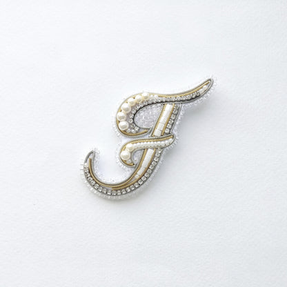 a decorative letter 'F' made of various materials, including pearls and beads, which are arranged in a visually appealing manner.