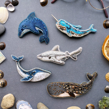 a collection of five intricately designed sea animal brooches, each with unique patterns and colors, arranged on a gray surface.