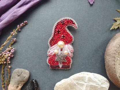 a red and white ornament with a gnome-like design, adorned with pearls and a star, placed on a gray background.