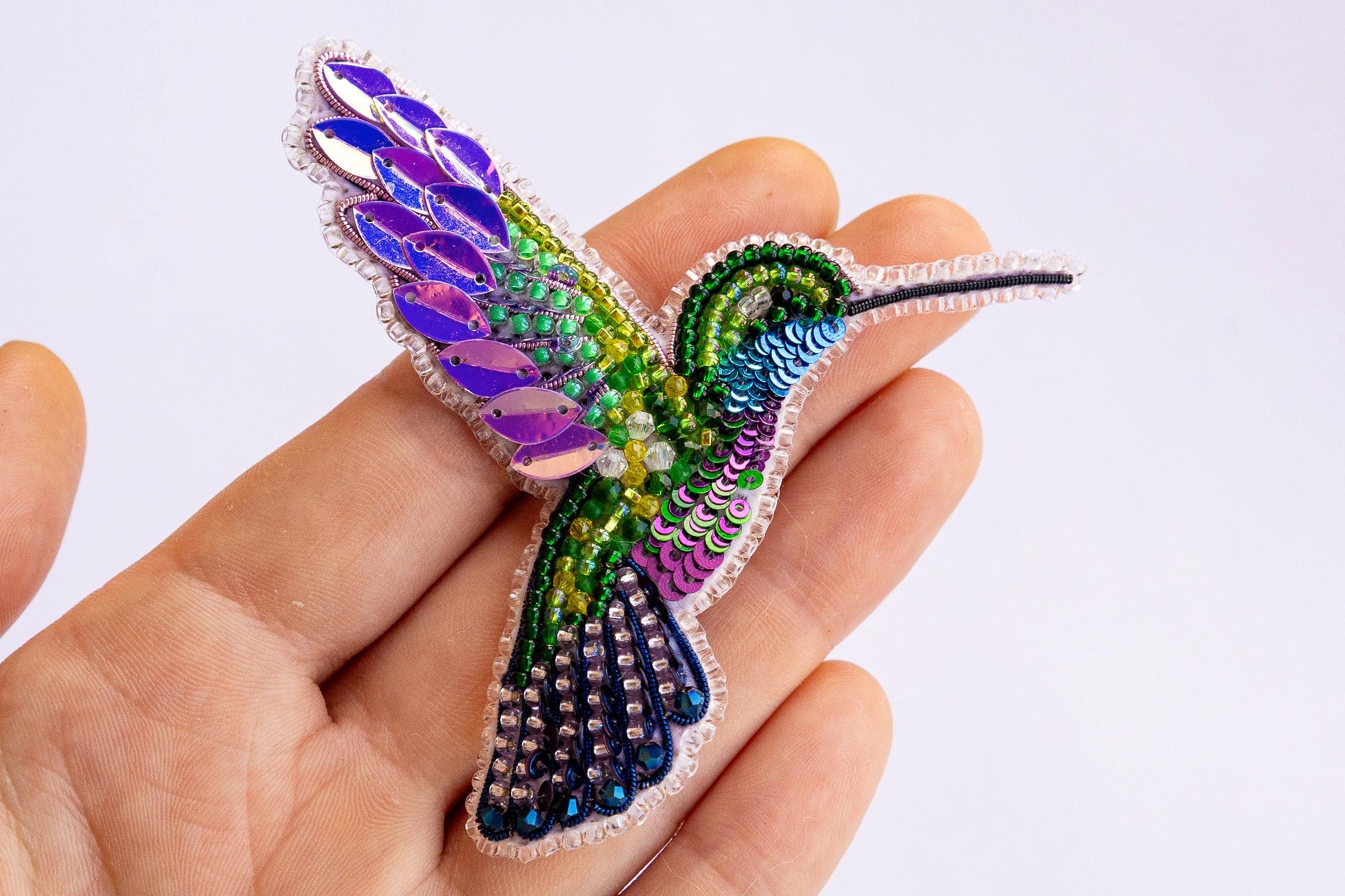 a colorful bird brooch sitting on top of a person&#39;s hand