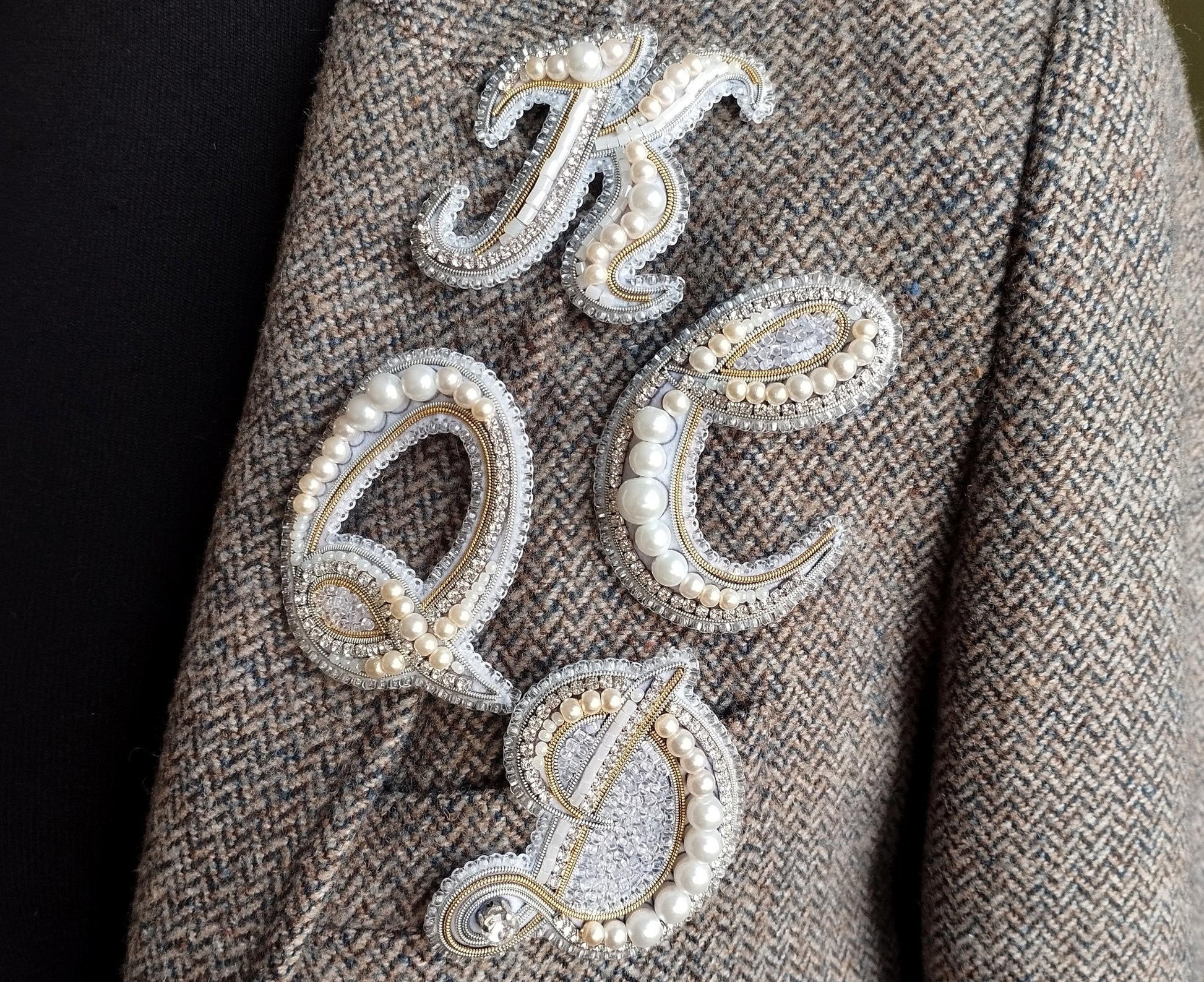 a close-up of a person's arm wearing a tweed jacket with a decorative embroidered letter on it.