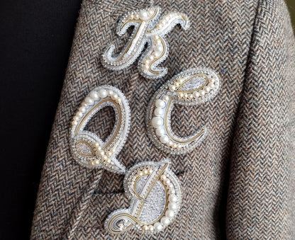 a close-up of a person's arm wearing a tweed jacket with a decorative embroidered letter on it.