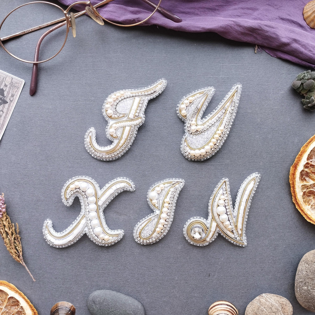 a collection of decorative elements arranged on a grey background, including a pair of glasses, a purple fabric, and various fruits and stones.