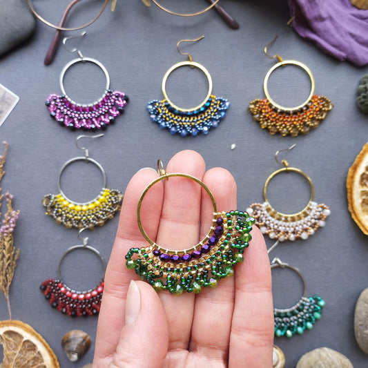 A hand holding a colorful beaded earring against a background of various other earrings and jewelry items.