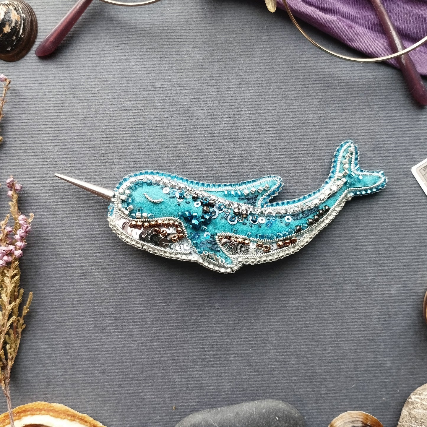 a blue and silver decorative object resembling a whale, placed on a gray surface surrounded by various objects.