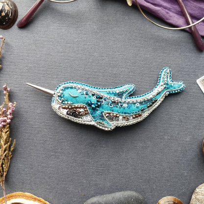 a blue and silver decorative object resembling a whale, placed on a gray surface surrounded by various objects.