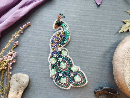a decorative peacock brooch with a vibrant and intricate design, surrounded by various natural elements such as flowers, leaves, and rocks.