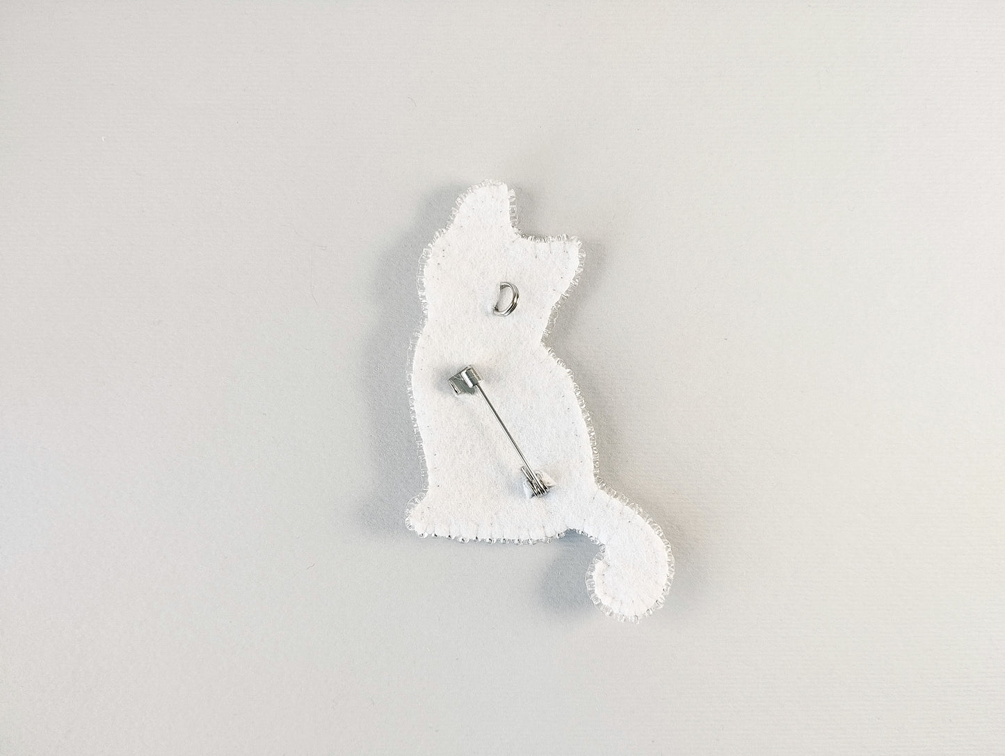 A white cat-shaped pin or badge is shown against a plain white background.