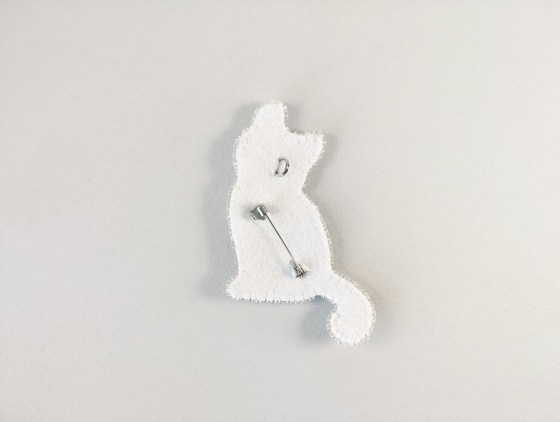 A white cat-shaped pin or badge is shown against a plain white background.