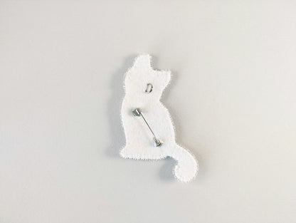 A white cat-shaped pin or badge is shown against a plain white background.