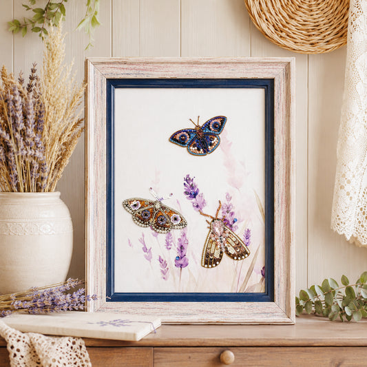 A framed painting of three butterflies, one blue and two brown, is displayed on a wooden surface, surrounded by various decorative elements such as a vase of dried flowers and a woven basket.