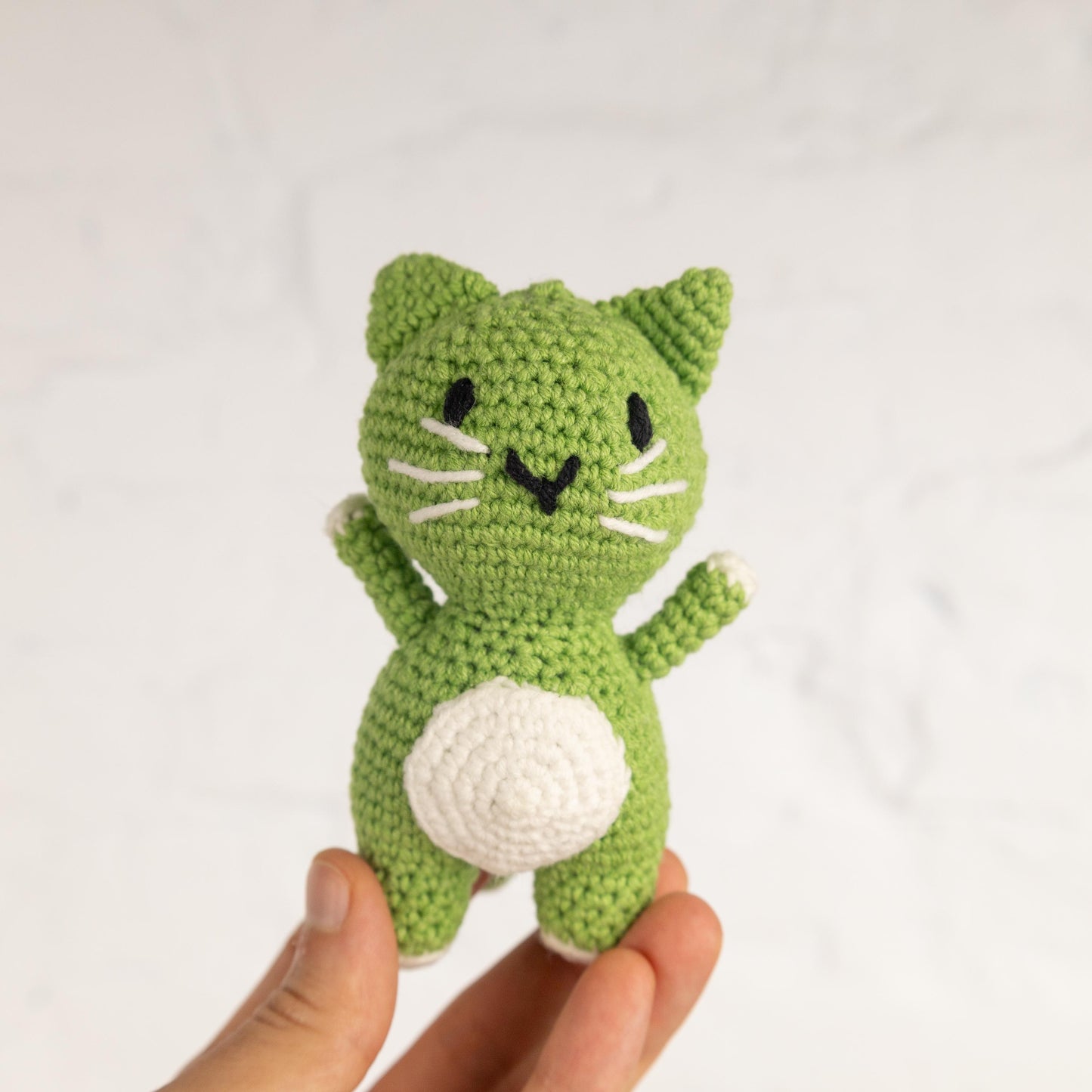 a hand holding a small green crocheted cat