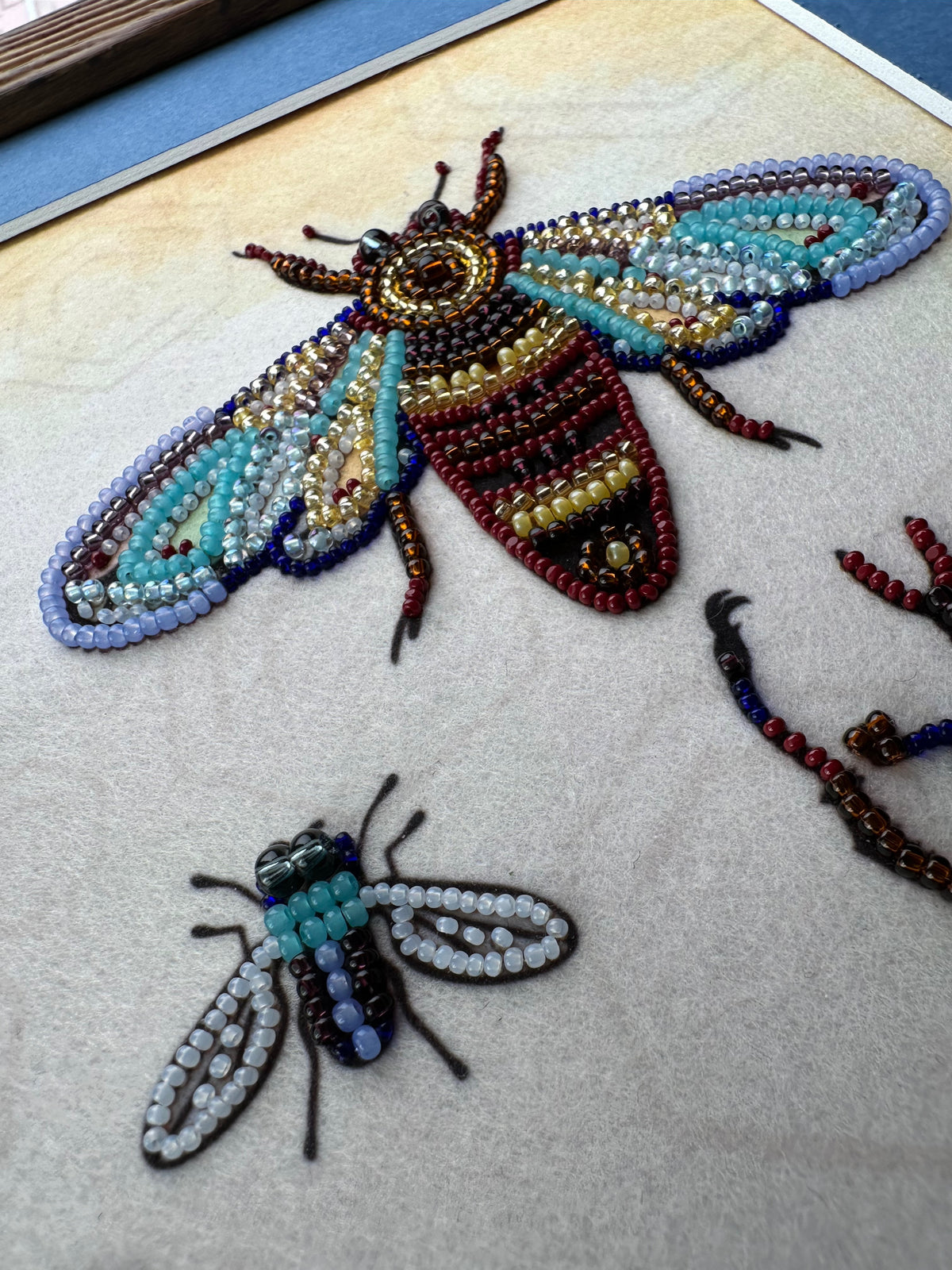 two intricately crafted insects, one larger and one smaller, both made from colorful beads and thread.
