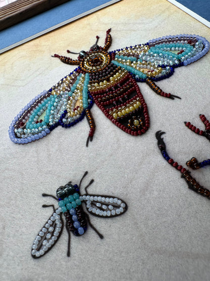 two intricately crafted insects, one larger and one smaller, both made from colorful beads and thread.